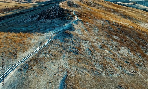 Aerial view of a snow dusted mountain with a winding path leading to the peak under a clear sky
