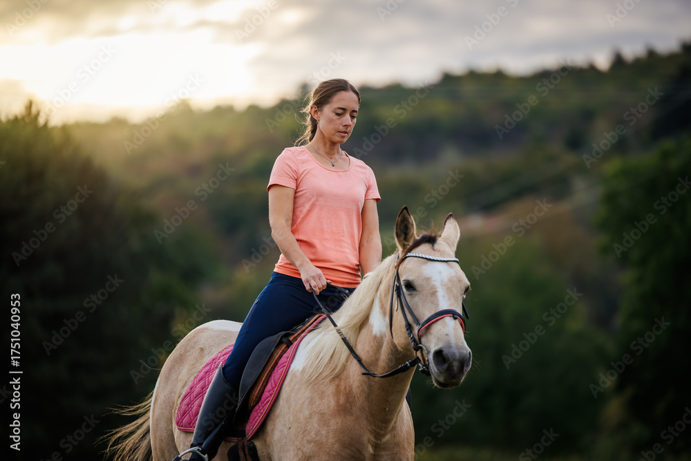 Obraz premium Woman riding horse during equestrian training session at sunset. Female rider practicing horseback riding