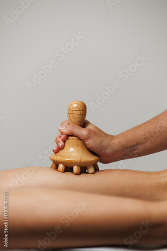 Close-up of wood therapy massage tool used on leg in wellness session.
