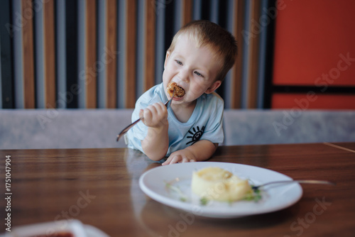 A little boy eating nuggets with mashed potatoes in a cafe