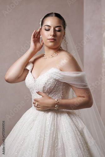 Elegant bride in stunning gown poses gracefully for wedding portraits in a soft-lit setting