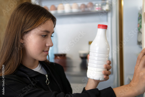 hungry girl open empty refrigerator. teen girl looks for food in the fridge and chooses what to eat. The girl takes out a white bottle of fresh milk from the refrigerator.