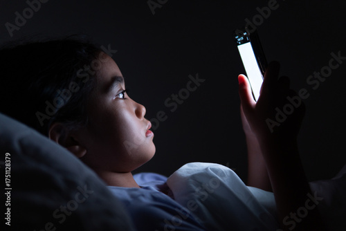 Child lying in bed using a smartphone at night. Screen time, insomnia, digital addiction concept.