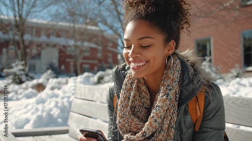 Female college student sitting on a bench at a university campus, checking her smartphone on a sunny winter day