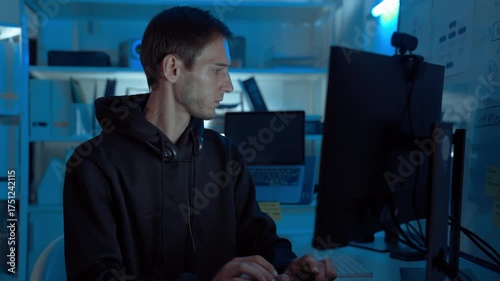 Professional male programmer working night shift in IT room, coding and testing software on multiple monitors, analyzing project data and debugging code, showcasing innovation and technology.