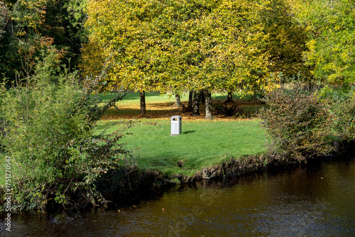 Riverbank Scene with Trees Grass and Litter Bin on an Autumn Morning