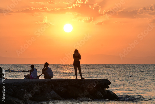 Paralia, Katerini, Greece, 14.08.2025: Sunrise over the sea in Paralia, Katerini, Greece. Silhouettes of people and a girl standing against the sun.