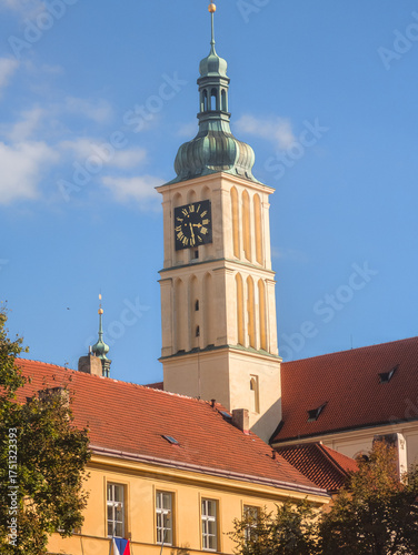 Majestic ancient clock tower of a historic cathedral with a golden spire under a clear blue sky in late summer, featuring warm yellow architecture and traditional red tiled roofs.