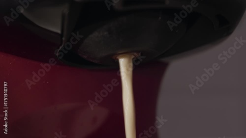 Coffee flows from capsule machine spout. Video footage of coffee streaming from the spout of a capsule coffee machine.