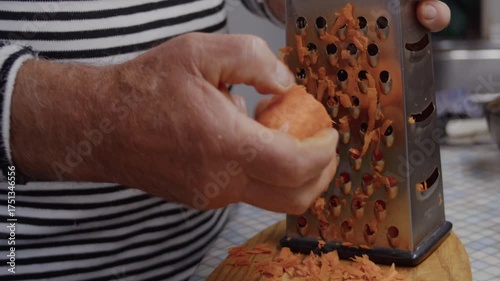 Close-up, hands of an elderly man grating raw carrots on kitchen table