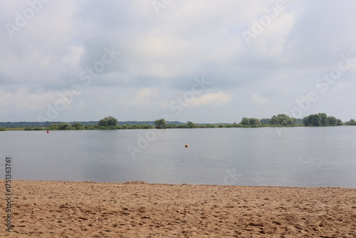 Experience the Serene Lakeside View Featuring a Sandy Beach Beneath a Cloudy Sky