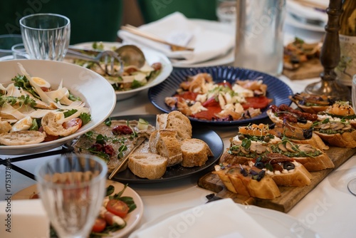 Appetizing Antipasto Table Spread Featuring Bruschetta, Salads, and Olives, Rustic Italian Cuisine, Dark Blue Plates, and White Linen.