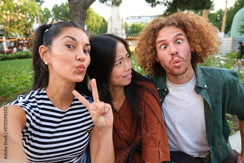 Three friends are making funny faces and taking a selfie in a park, enjoying their time together