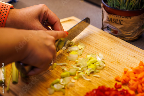 Woman expertly slicing fresh leeks on wooden board for healthy meal preparation