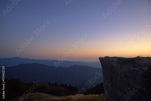  夕焼け空と山並みを見下ろす巨岩の先端