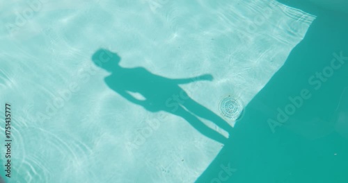 Shadow of a woman standing by a pool on a sunny day. 