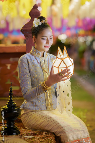 Pretty Asian woman in Thai traditional costume in the Hundred Thousand Lantern Festival or Yi Peng Festival for worship at Phra That Hariphunchai temple in Lamphun, Thailand.