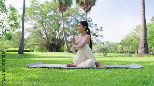 Beautiful young Asian woman practicing yoga outdoors on sunny day at public park.Serene female peaceful and mindfulness sit on exercise mat make lotus pose