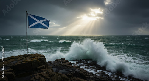 The Scottish flag flies on a rocky coast during a dramatic storm. Powerful ocean waves crash as sunbeams break through dark clouds over Scotland