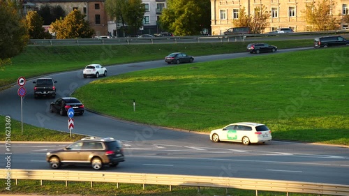Cars moving through curved road interchange with green grass median in evening light showing organized traffic system, transportation infrastructure and modern city road planning