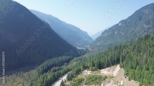 Cinematic drone footage captures the epic scale of a remote mountain pass. The camera flies high above the forest, revealing the winding road and clear-cut areas below.
