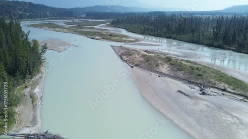 Cinematic aerial footage follows the course of a wild, untamed river. The camera glides over the braided channels, showcasing the vast and rugged beauty of the untouched wilderness.