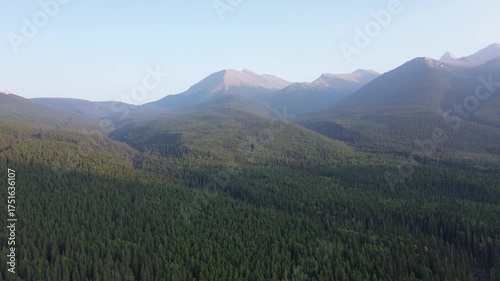 Cinematic drone footage captures the immense scale of a remote mountain wilderness. The sun's first light illuminates the misty peaks and the endless sea of green treetops below.