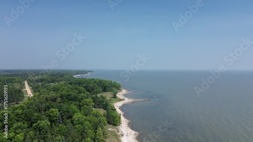 This cinematic drone footage follows a remote coastal road beside a pristine beach. The path winds through lush woods, evoking a sense of adventure, road trips, and peaceful travel.