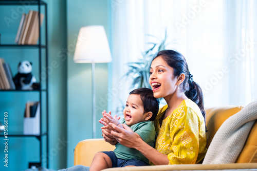 Fotografie Indian young mother and infant baby clapping on sofa while cuddling and playing