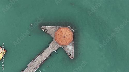 A sweeping aerial video showcasing Qingdao's Zhanqiao Pier leading to the historic Huilan Pavilion, with tranquil turquoise waters and scattered boats.