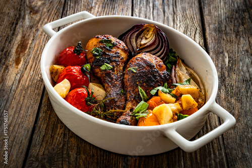Roasted chicken drumsticks and vegetables in baking dish on wooden table