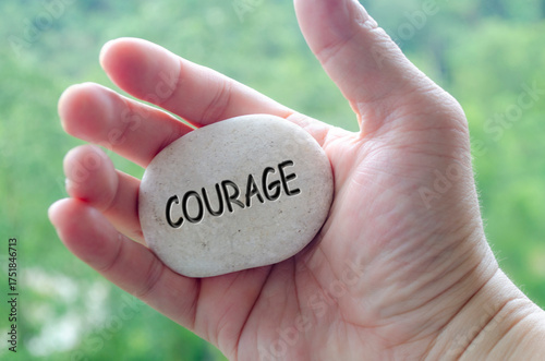 Hand holding a white stone with COURAGE text engraved on it, embodying life purpose of bravery and confidence in challenges.