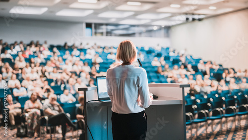Female speaker giving a talk on corporate business conference. Unrecognizable people in audience at conference hall. Business and Entrepreneurship event
