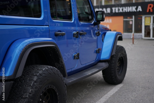 Blue off-road vehicle parked in a city area with shops nearby during the day