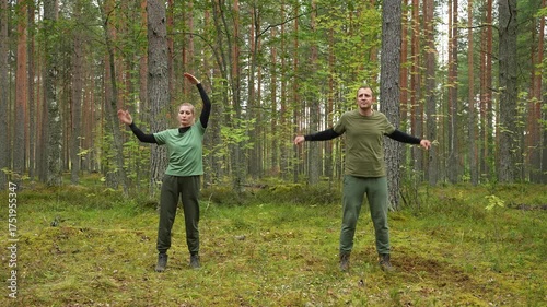 Man and woman warm up in a pine forest. They perform outdoor stretching and light calisthenics. Morning workout during camping. Natural ambient setting. Active outdoor recreation.
