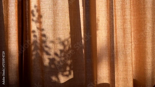 Dynamic play of light and shadow: mesmerizing movement of plant shadows dancing on translucent orange linen curtains, creating a serene and natural ambiance in a sunlit room.Gentle morning light