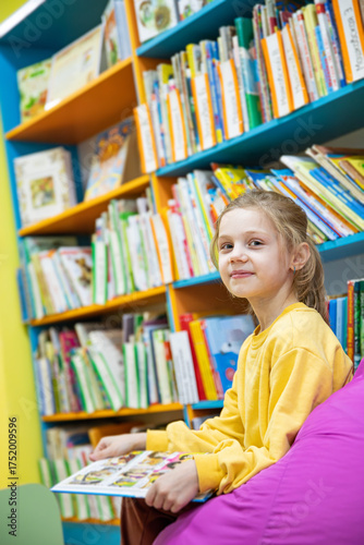 Portrait of a 7-8-year-old blonde girl in a yellow longsleeve in a library with books