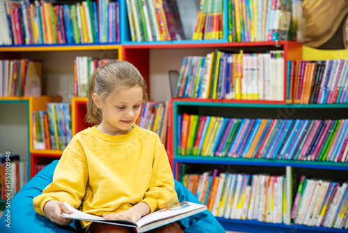 Portrait of a 7-8-year-old blonde girl in a yellow longsleeve in a library with books