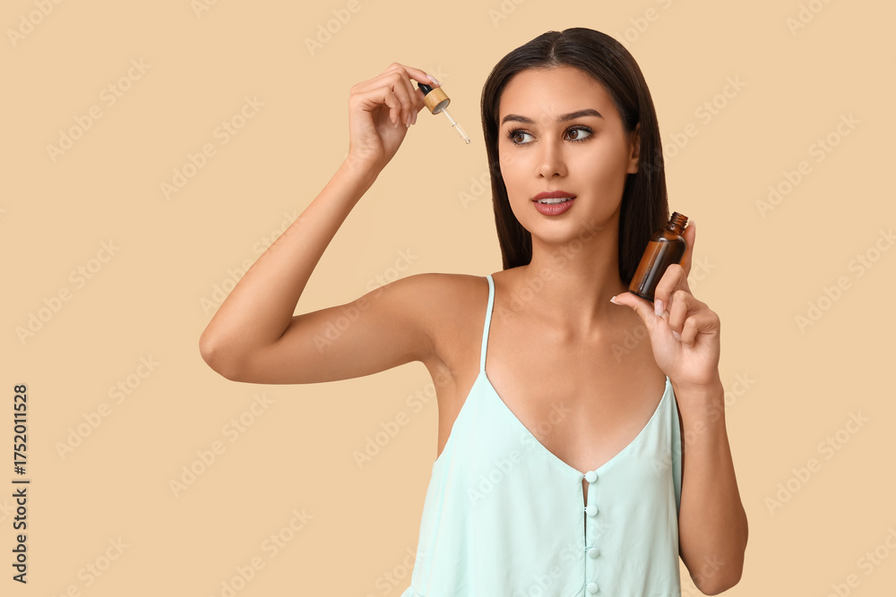 Fototapeta premium Beautiful woman holding serum with vitamin E on beige background