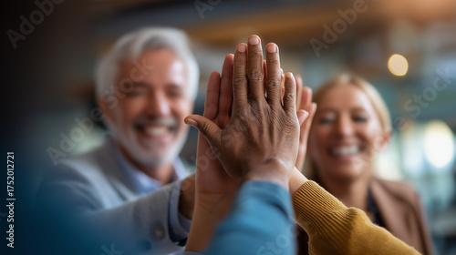Excited diverse employees giving high five to elder boss hands central faces out open office intentionally defocused team celebration faceless background defocused morale boo