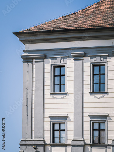 Close-up of a historic building facade in the old town of Cakovec, Croatia. Elegant architectural details and soft gray tones highlight the classic European design under a clear blue sky.