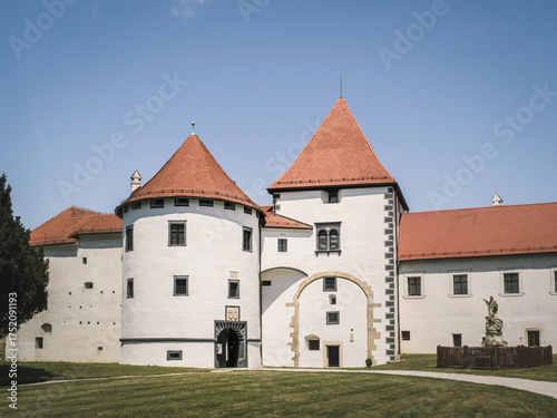 A view of Varazdin Castle in Croatia with its white walls, red rooftops, and blue sky. The well-preserved fortress is a major landmark showcasing Renaissance architectural elegance.