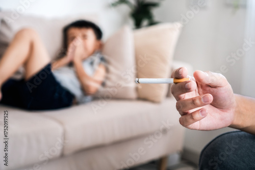 Asian father smoking next to his young son, The child covers his nose to avoid the cigarette smell, showing the dangerous effects of secondhand smoke and bad habits at home. 