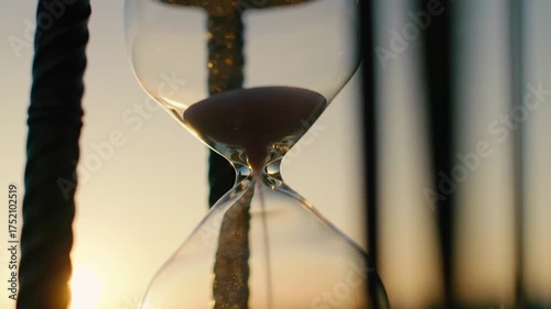 An hourglass with sand flowing through it, set against a backdrop of a sunset.