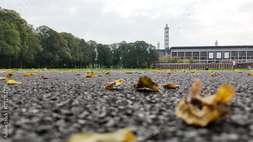 Cologne, Germany - 12 October, 2025: Wide lawn in front of a modern football stadium in Muengersdorf under cloudy sky. Long facade with brick pavilions and trees. Urban park sports venue. No people.