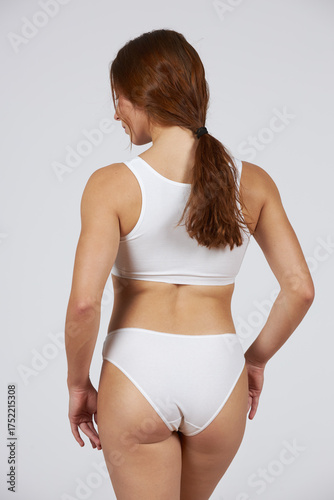 Young beautiful girl in white lingerie stands with his back on a gray background