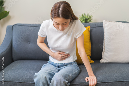 Quadro su tela Sick asian young woman in pain, hand holding belly, stomach pain from food poisoning, girl hurt abdomen ache and digestive problem, gastritis or diarrhea
