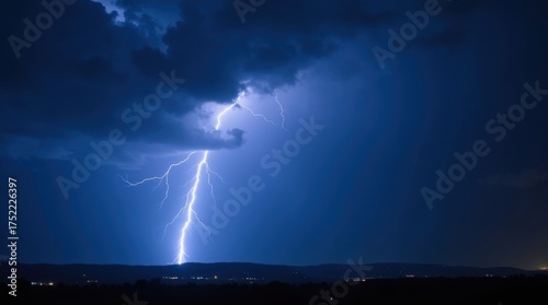 Intense blue lightning strike illuminating dark stormy clouds over a distant landscape