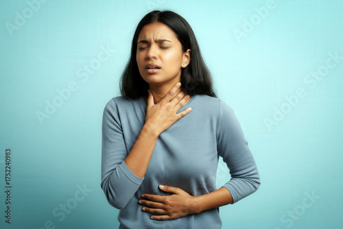 Medical Illnesses and Ailments – Young adult Indian woman clutching throat and stomach, experiencing severe acid reflux pain.