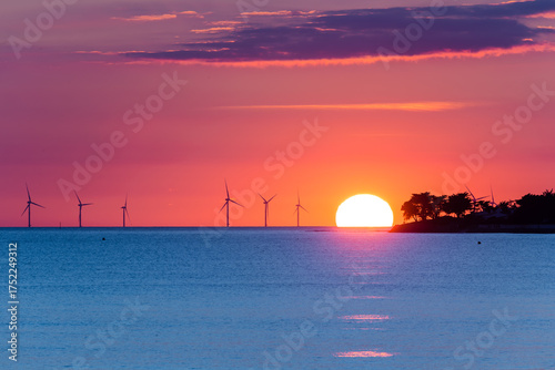 Fotomural Éoliennes offshore au soleil couchant encore visible au dessus de l'horizon